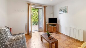 Un salon comprenant un canapé, une table basse avec une plante, un téléviseur posé sur un meuble et une porte-fenêtre coulissante donnant sur un espace extérieur.