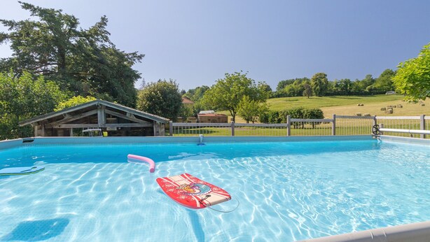 Une piscine avec une eau d’un bleu limpide, un flotteur rouge et, au fond, un bâtiment en bois.