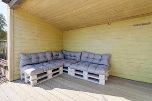 Ett takförsett utomhusområde med sittplatser, ett träbeklätt tak och väggar, en modulsoffa och ett trädäck.
