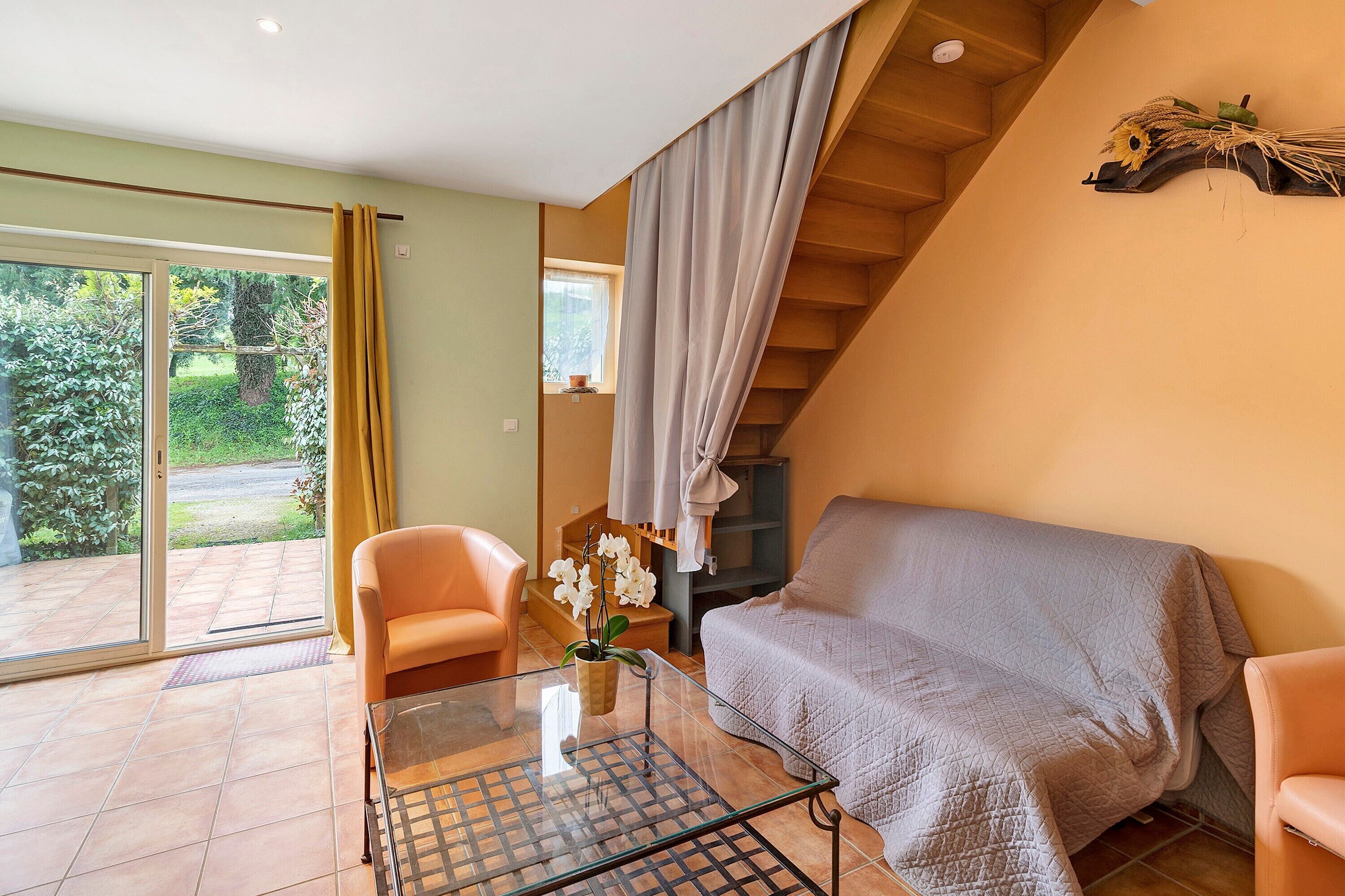 A room with a glass table, a sofa, a chair, a potted plant, and a staircase.
