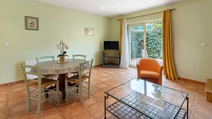 Een eethoek met een tafel, stoelen, een glazen salontafel, een televisie en een raam met gordijnen.