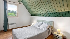 Een slaapkamer met een bed, nachtkastje, lamp, raam en houten plafond.