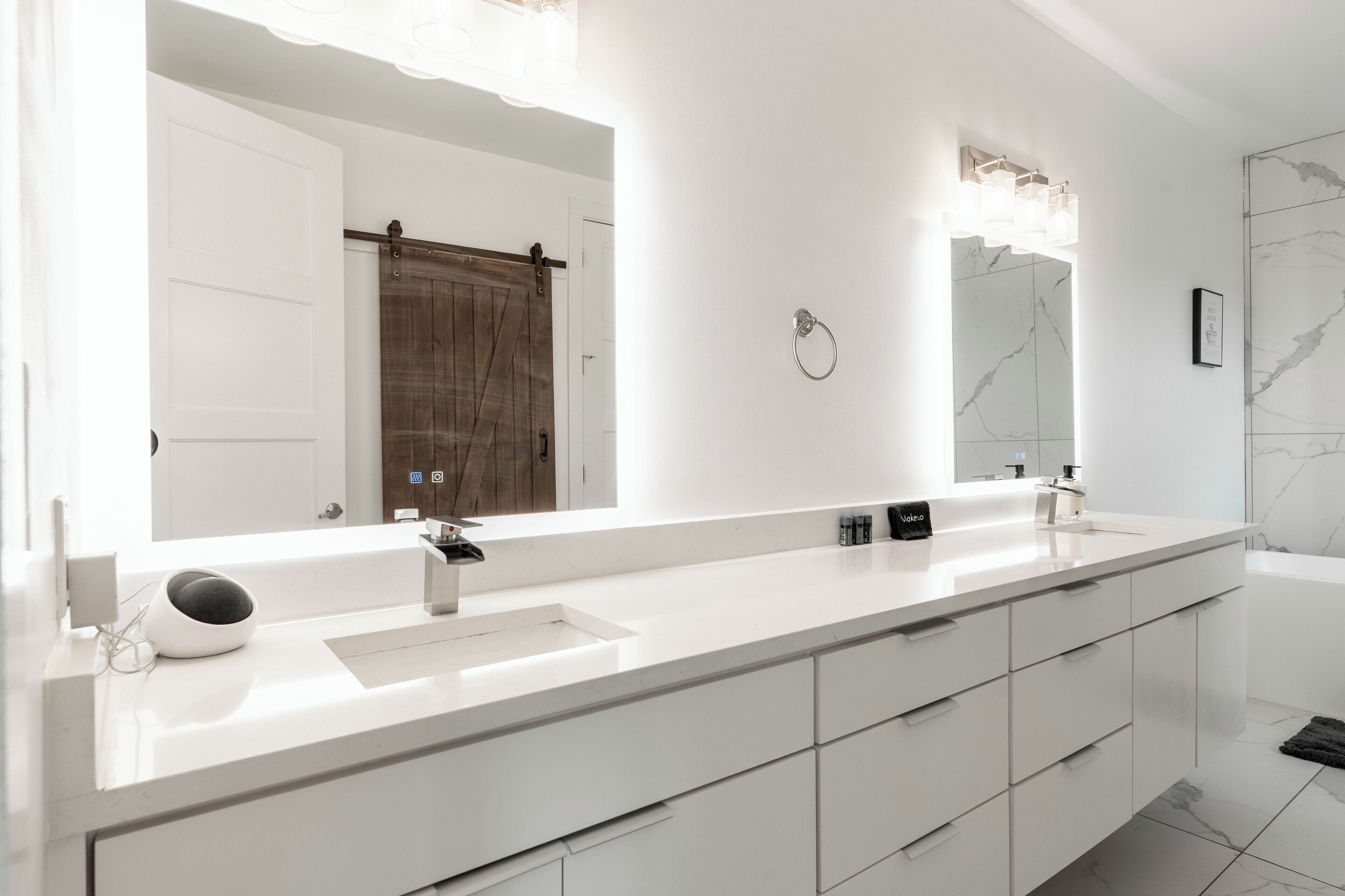 A modern bathroom with a white vanity, a large mirror, and a marble backsplash.