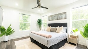 Ein modernes Schlafzimmer mit einem großen Bett, einem Deckenventilator und zwei Fenstern.