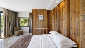 A modern bedroom with a wooden accent wall, a large bed, a chair, and a window with curtains. - Holiday Home “Loft 2 – Sea View with Pool”, Wi-Fi and Air Conditioning (Porto-Vecchio)