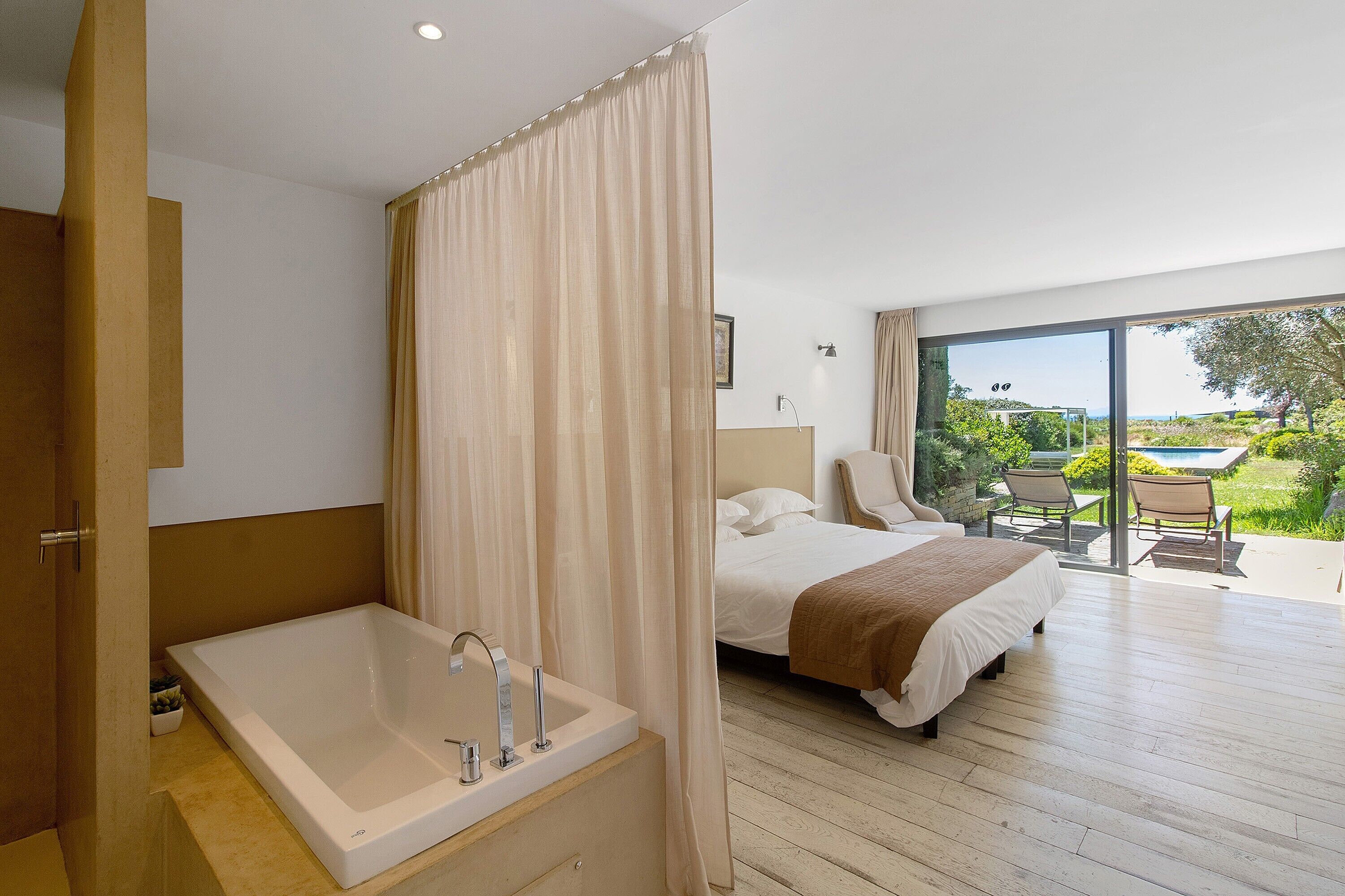 Ein modernes Hotelzimmer mit einer großen Badewanne, einem Bett mit Gartenblick und einem Balkon mit Sitzgelegenheit.