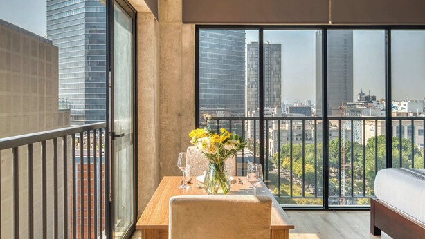 Een balkon met een eettafel, stoelen, een vaas met bloemen en uitzicht over de stad.