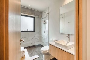 Une salle de bain moderne avec une douche en marbre, des toilettes blanches, un lavabo avec un miroir et un porte-serviettes.