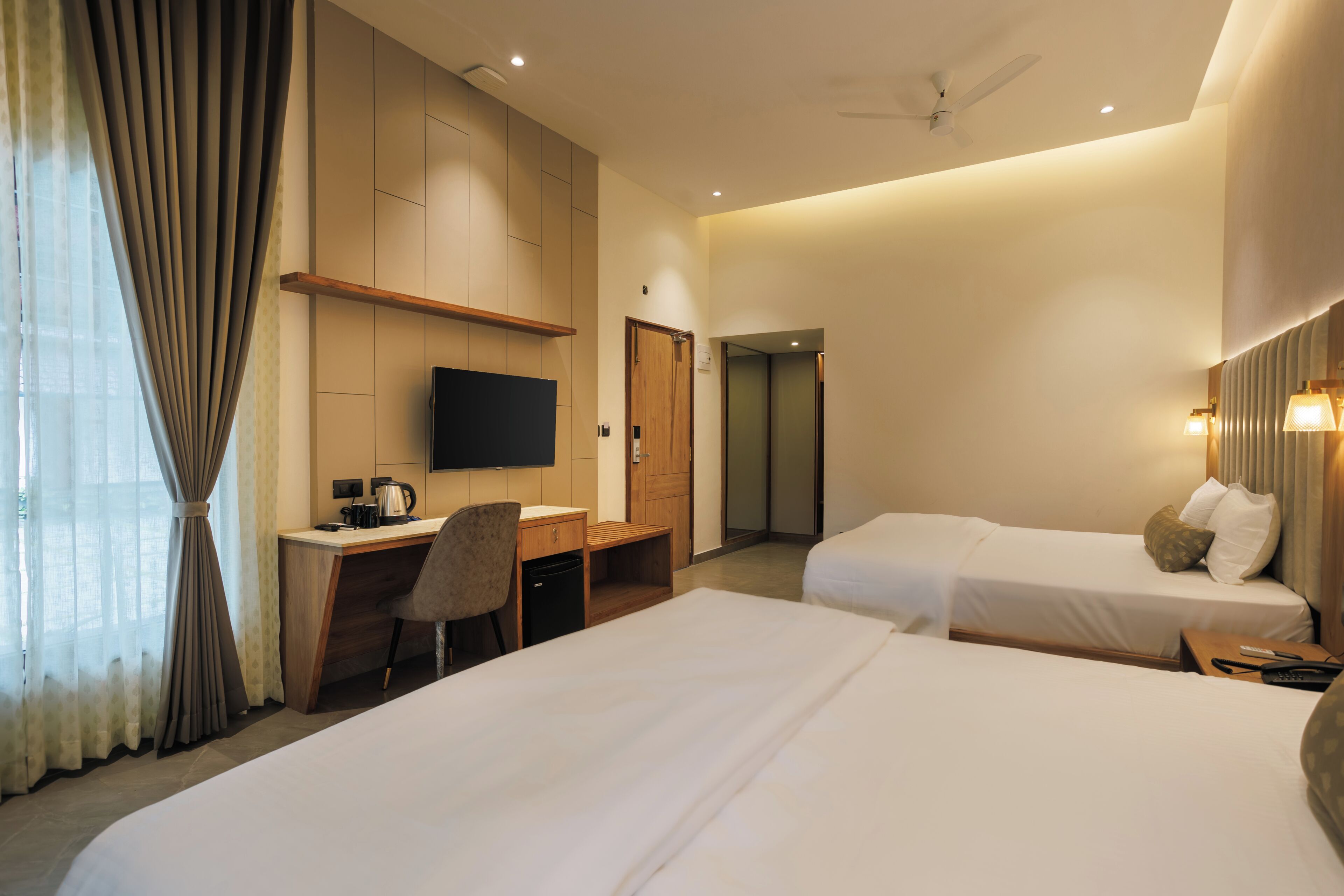 A hotel room with two beds, a desk, a television, and a shower area.