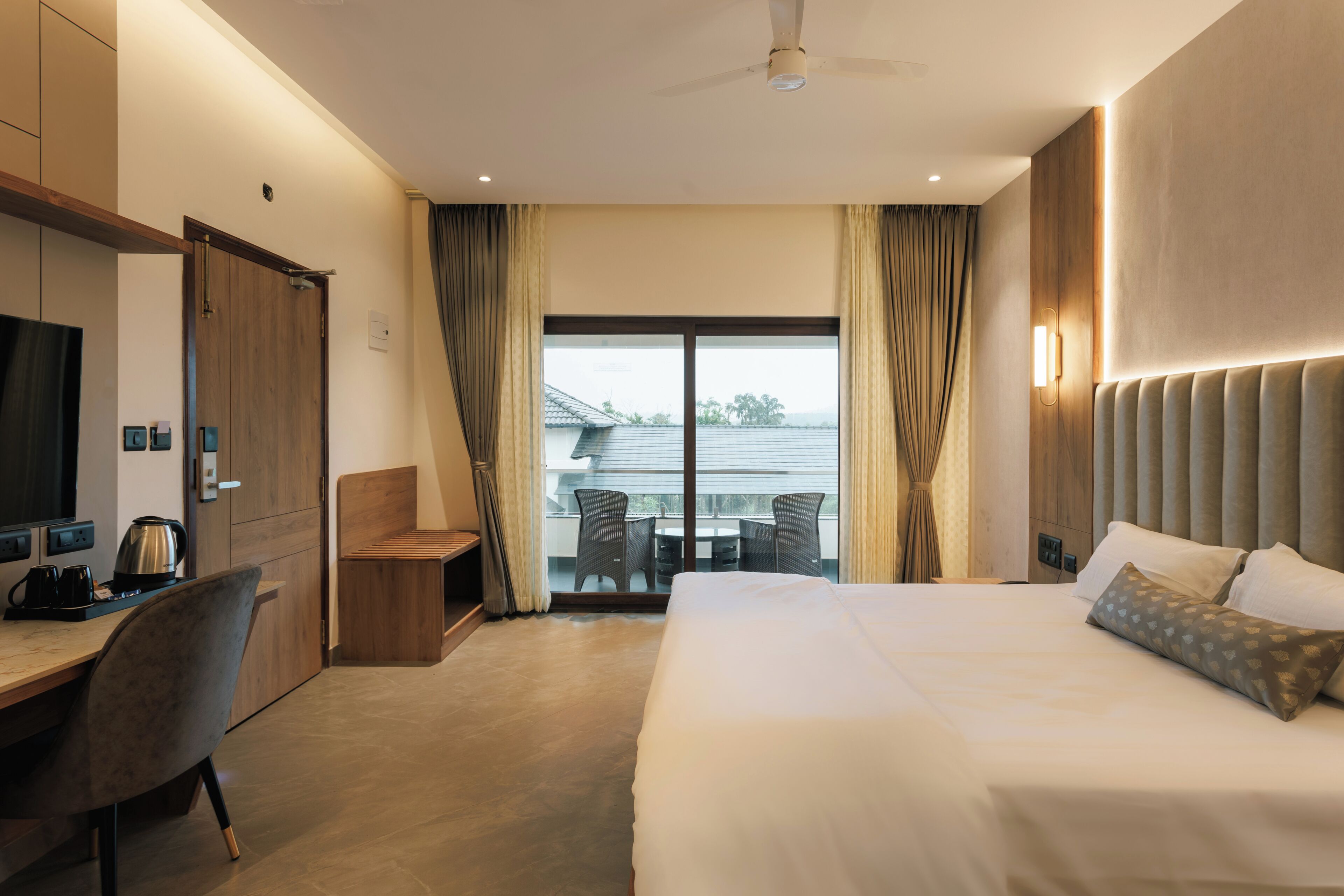 A hotel room with a bed, a desk, a chair, a television, and a balcony with curtains.