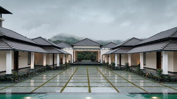 Ein Hotel mit zentralem Pool, mehreren Zimmern mit Ziegeldächern und Blick auf die Berge im Hintergrund.