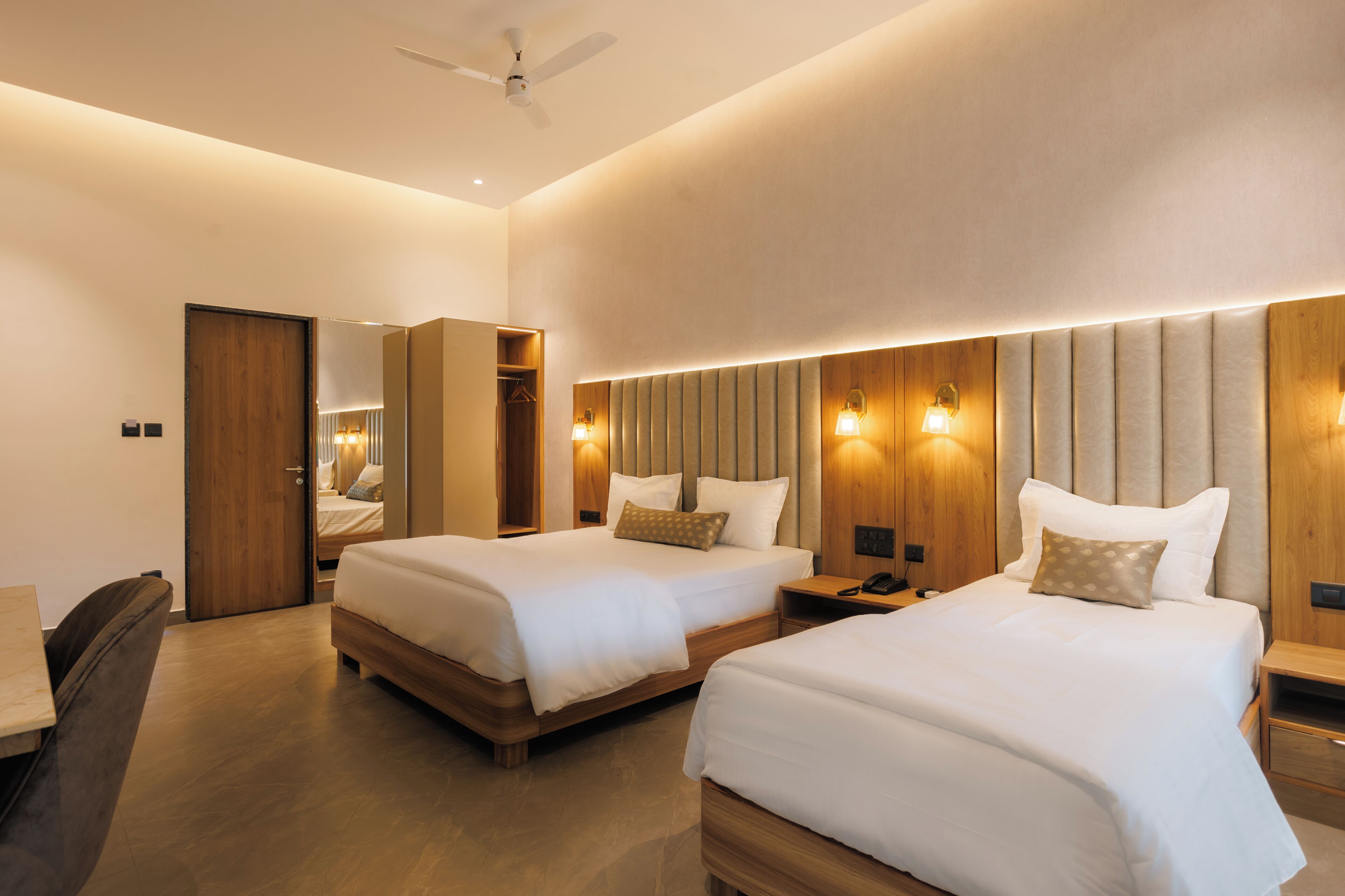 Quarto de hotel com duas camas, um guarda-roupa, um espelho e um ventilador de teto.