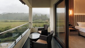 Ein Balkon mit Korbmöbeln, einem Bett und Blick auf eine grüne Landschaft.