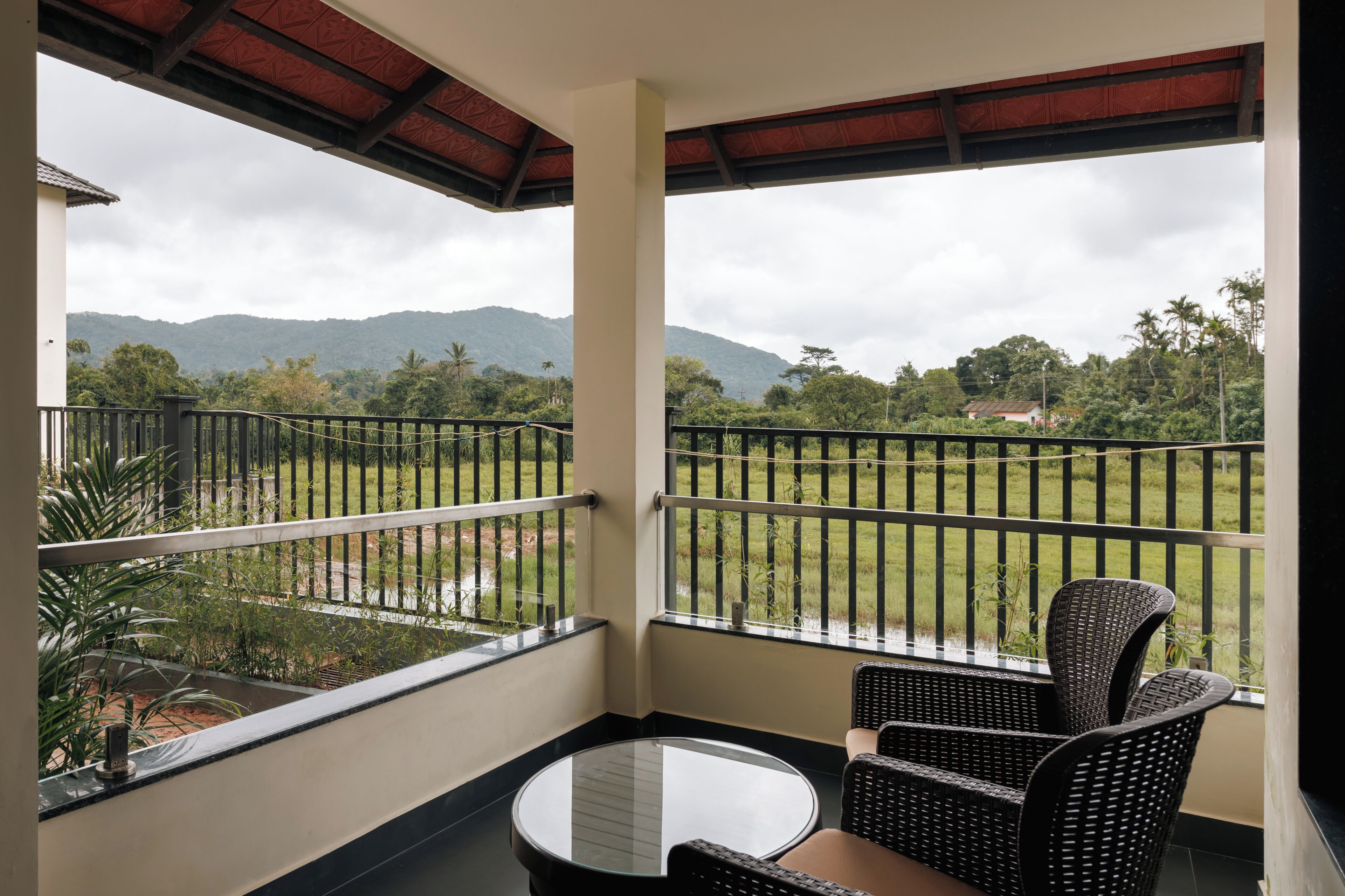 A balcony with a table and chairs, offering a view of a lush landscape and distant mountains.