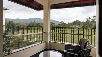 A balcony with a table and chairs, offering a view of a lush landscape and distant mountains.
