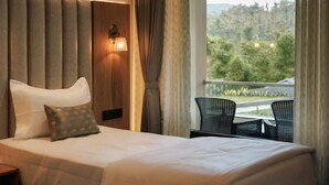 Ein Hotelzimmer mit Bett, Nachttisch, Wandlampe und Blick ins Freie durch ein Fenster.
