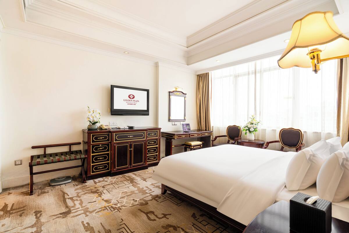 Habitación de hotel con una cama grande, un escritorio con silla, una tocador con espejo y un banco.