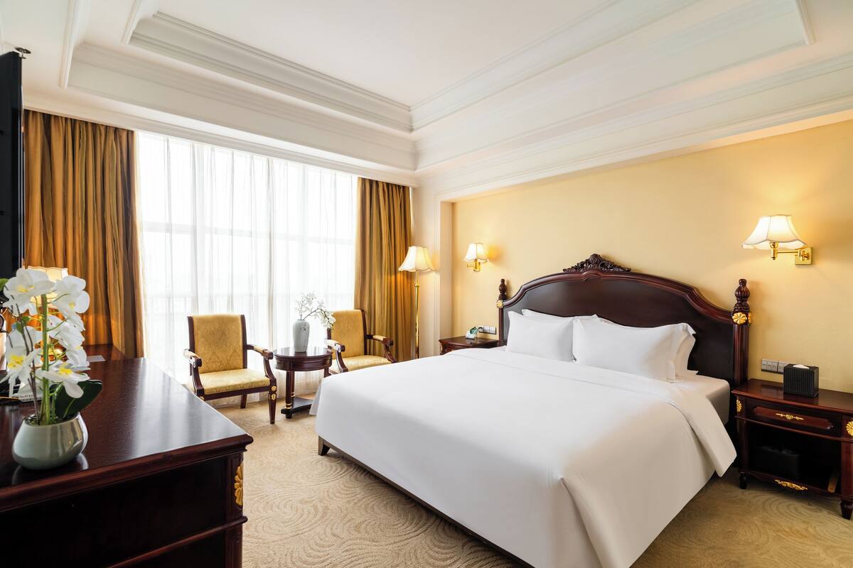 Habitación de hotel con una cama grande, un escritorio con un florero, una silla y una mesita.
