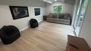 A modern living room with a sofa, bean bag, and a remote control on a wooden table. - Recently Renovated Lakefront Retreat on George Lake (Fairmont)