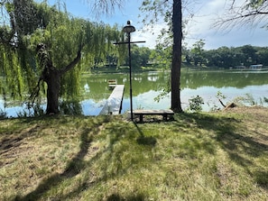 A lakeside park with a wooden dock, a bench, and a lamppost.