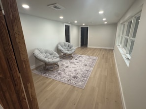 Una habitación amplia con dos sillones tapizados, un alfombra estampado, suelo de madera y una ventana con persianas.