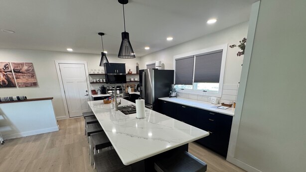A modern kitchen with a central island, bar stools, pendant lighting, and a view of the outdoors. - Recently Renovated Lakefront Retreat on George Lake (Fairmont)
