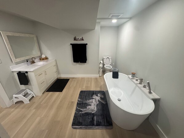 Een moderne badkamer met een vrijstaand bad, een wastafel met spiegel, een toilet en een zwart tapijt met een hertenprint.