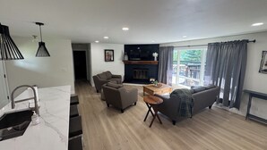 A modern living room with a fireplace, a sofa, a coffee table, and a dining area with a kitchen counter. - Recently Renovated Lakefront Retreat on George Lake (Fairmont)
