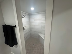 A bathroom with white tiled walls, a shower, and a bathtub.