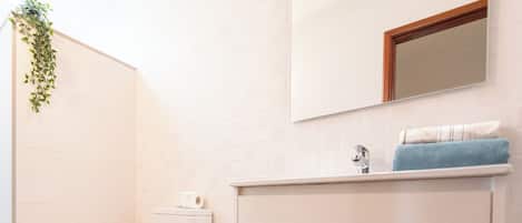 A bathroom with a toilet, sink, mirror, and a trash bin.