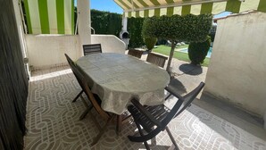 Une terrasse extérieure avec une table et des chaises, un auvent à rayures et une vue sur une piscine et un jardin.