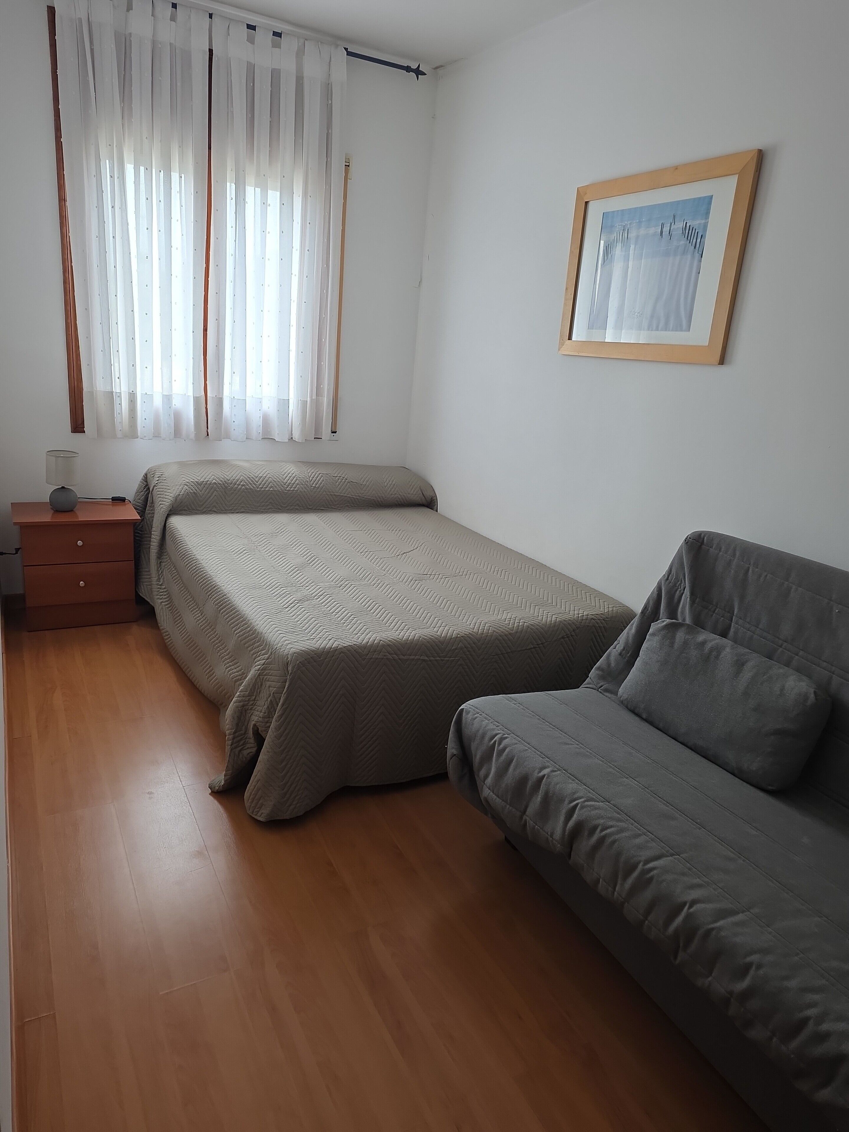 Habitación con dos camas, un sofá, una mesita de noche y un cuadro en la pared.