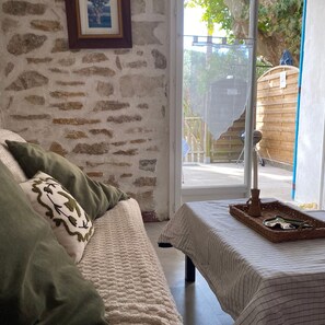 Una habitación acogedora con pared de piedra, una cama con almohadas verdes y blancas, una ventana que ofrece vistas al exterior y una mesa con una bandeja.