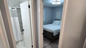 Ein schmaler Korridor mit Holzboden, der in ein Schlafzimmer mit Bett und Nachttisch führt.
