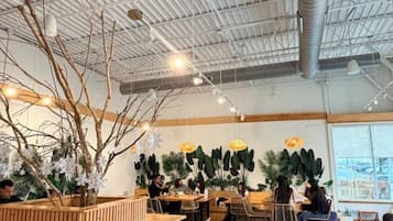 An indoor space with a high ceiling, exposed ductwork, and a central wooden counter with seating.