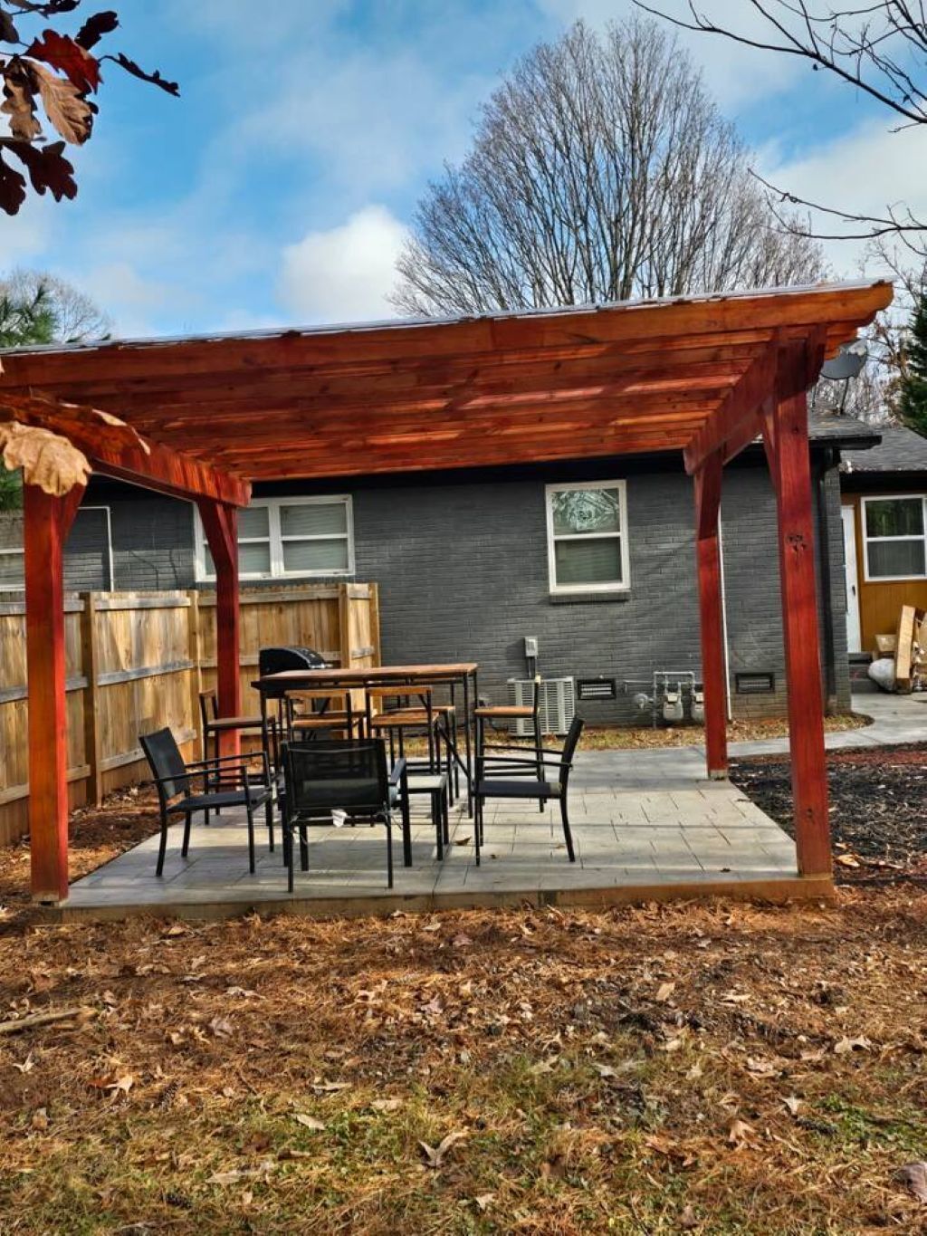 A covered patio area with a wooden pergola, a table, and chairs.