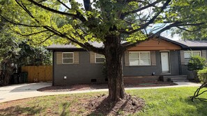 Une maison d’habitation avec un grand arbre devant, une pelouse ombragée et une boîte aux lettres bien visible.