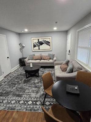 A modern living room with a grey sofa, a coffee table, and a dining table with chairs. - Charlotte Cozy Charm: Cozy Retreat with BBQ Oasis (Charlotte)