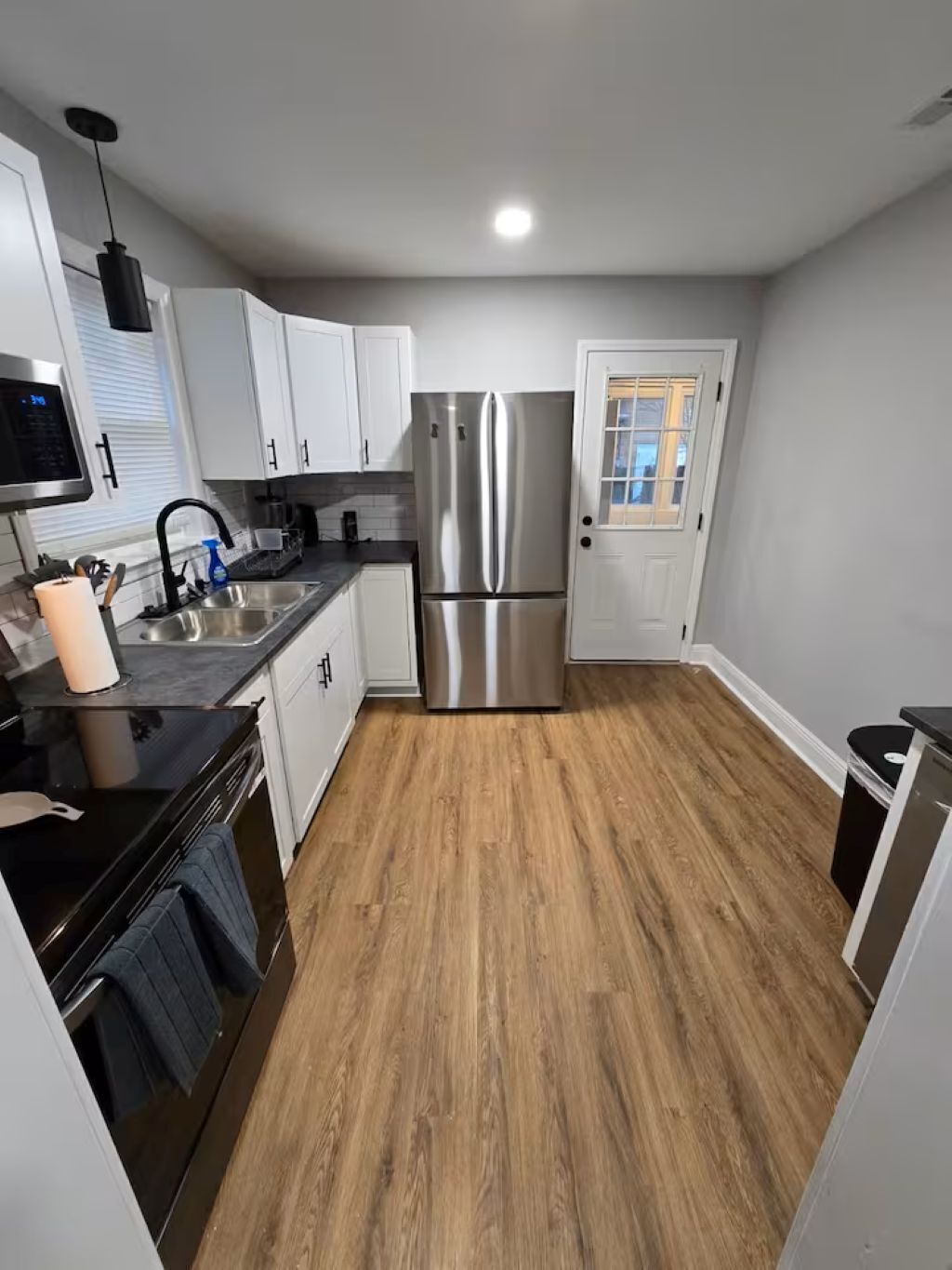 A modern kitchen with white cabinets, a stainless steel refrigerator, and a wooden floor.