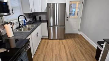 A modern kitchen with white cabinets, a stainless steel refrigerator, and a wooden floor.