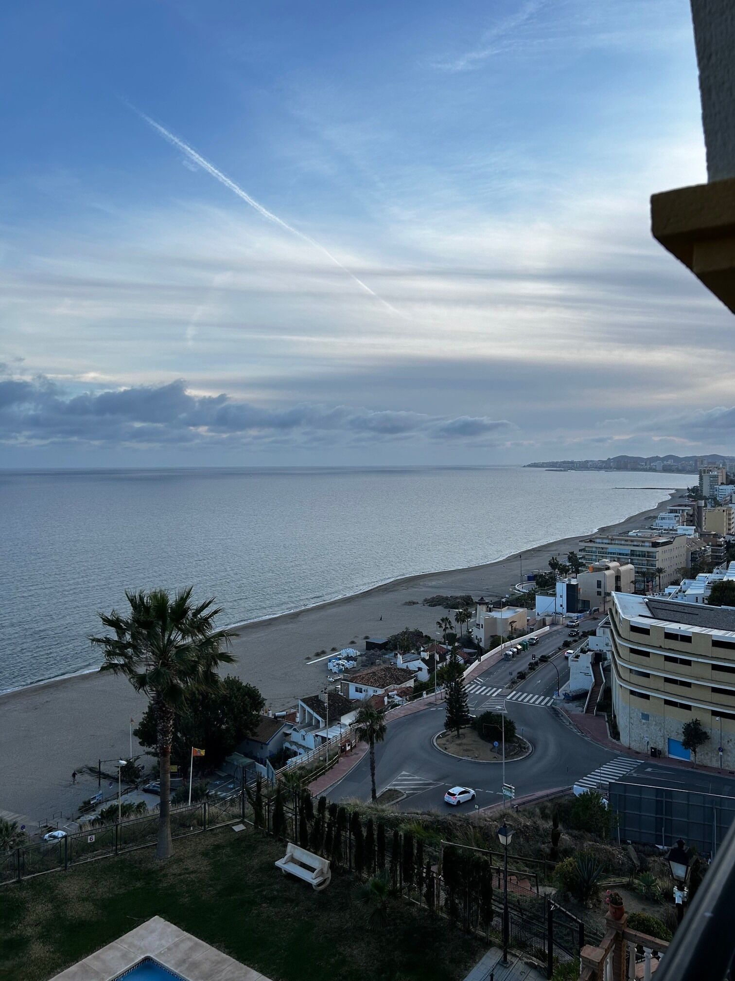 A coastal cityscape with a view of the sea, buildings, and a road leading to the beach.