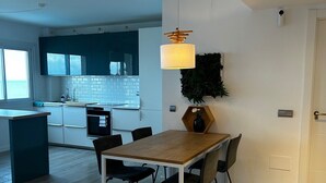 Una cocina moderna con comedor, que incluye una mesa y sillas de madera, una lámpara colgante y vistas a la cocina a través de una ventana.