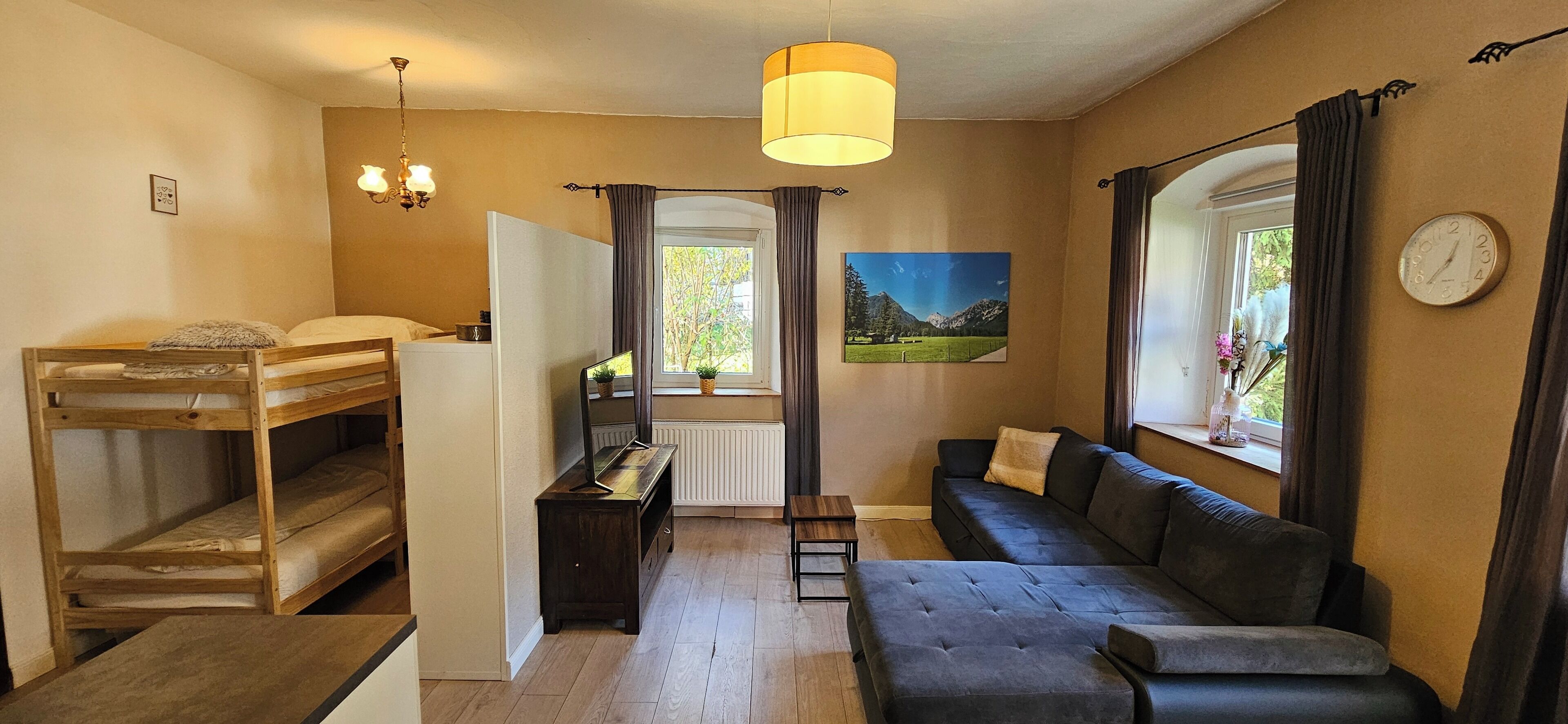 Een kleine kamer met een stapelbed, een slaapbank, een tafeltje en een spiegel.