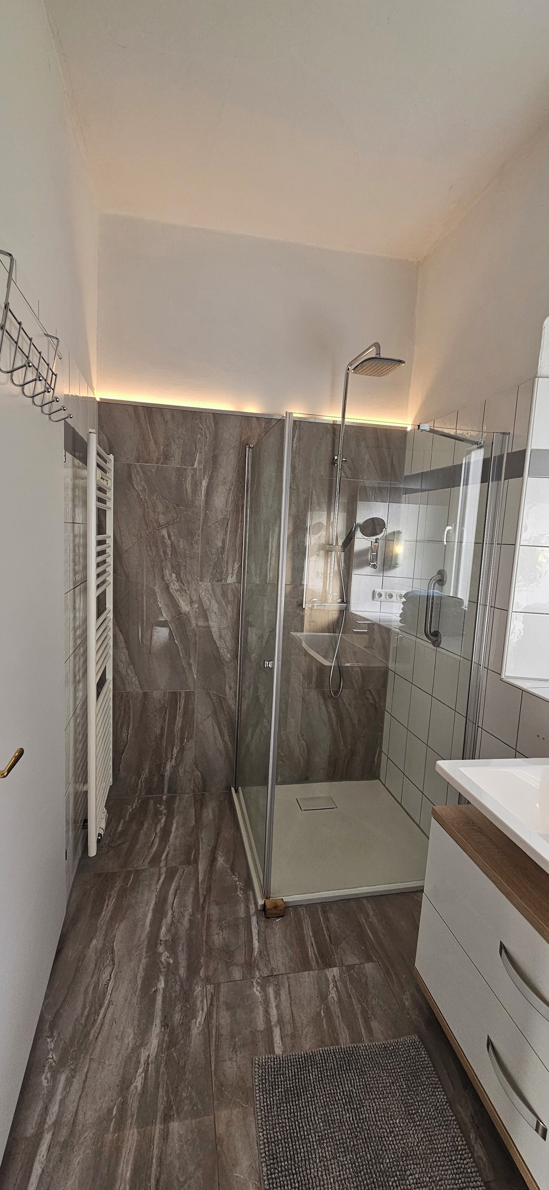 Een moderne badkamer met een douchecabine van glas, een witte wastafel en een vloer betegeld met marmer.
