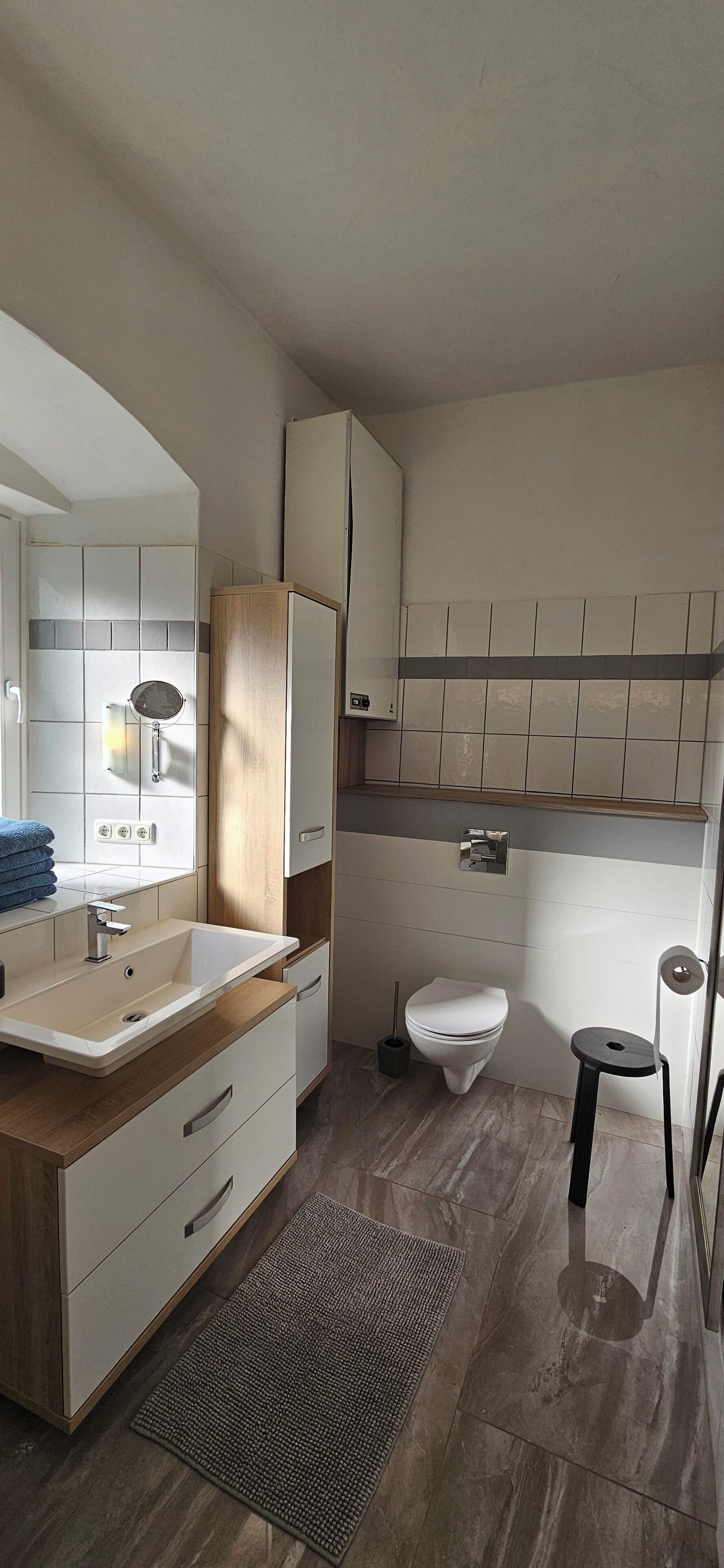 Un baño moderno con tocador de madera, un lavamanos, un inodoro y un taburete pequeño.