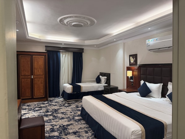 Una habitación de hotel con una cama grande, dos camas más pequeñas, un escritorio, un armario y un baño.