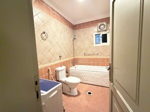 A bathroom with a toilet, a bathtub, and a washing machine. - Akarem Al Slamah Serviced apartments (Al Quwaiiyah)