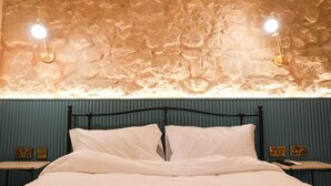A bed with white linens, a black metal headboard, and two bedside tables with lamps. - Fourteen Guesthouse  (Żejtun)