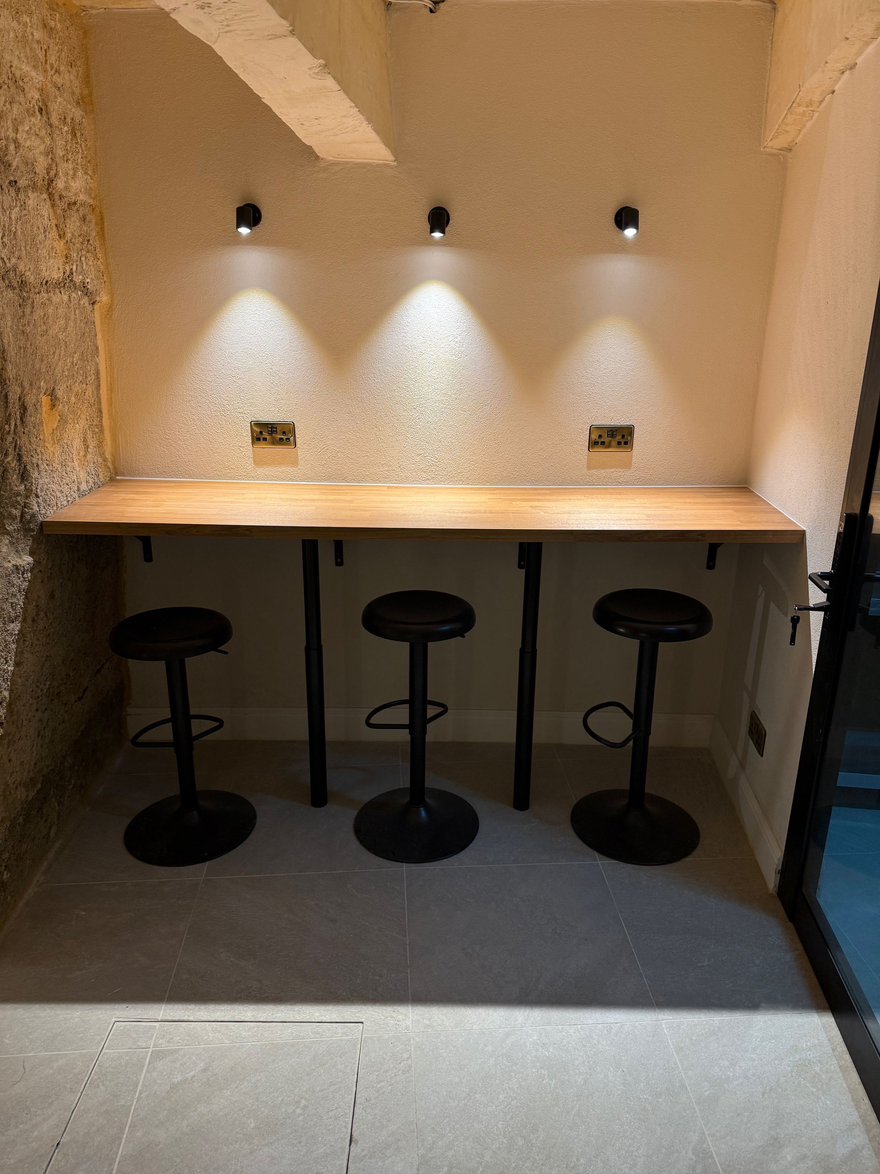 A bar area with a wooden countertop and three black stools.