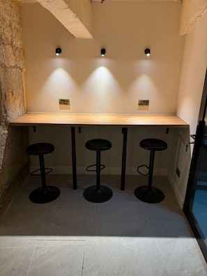 A bar area with a wooden countertop and three black stools. - Fourteen Guesthouse (Żejtun)